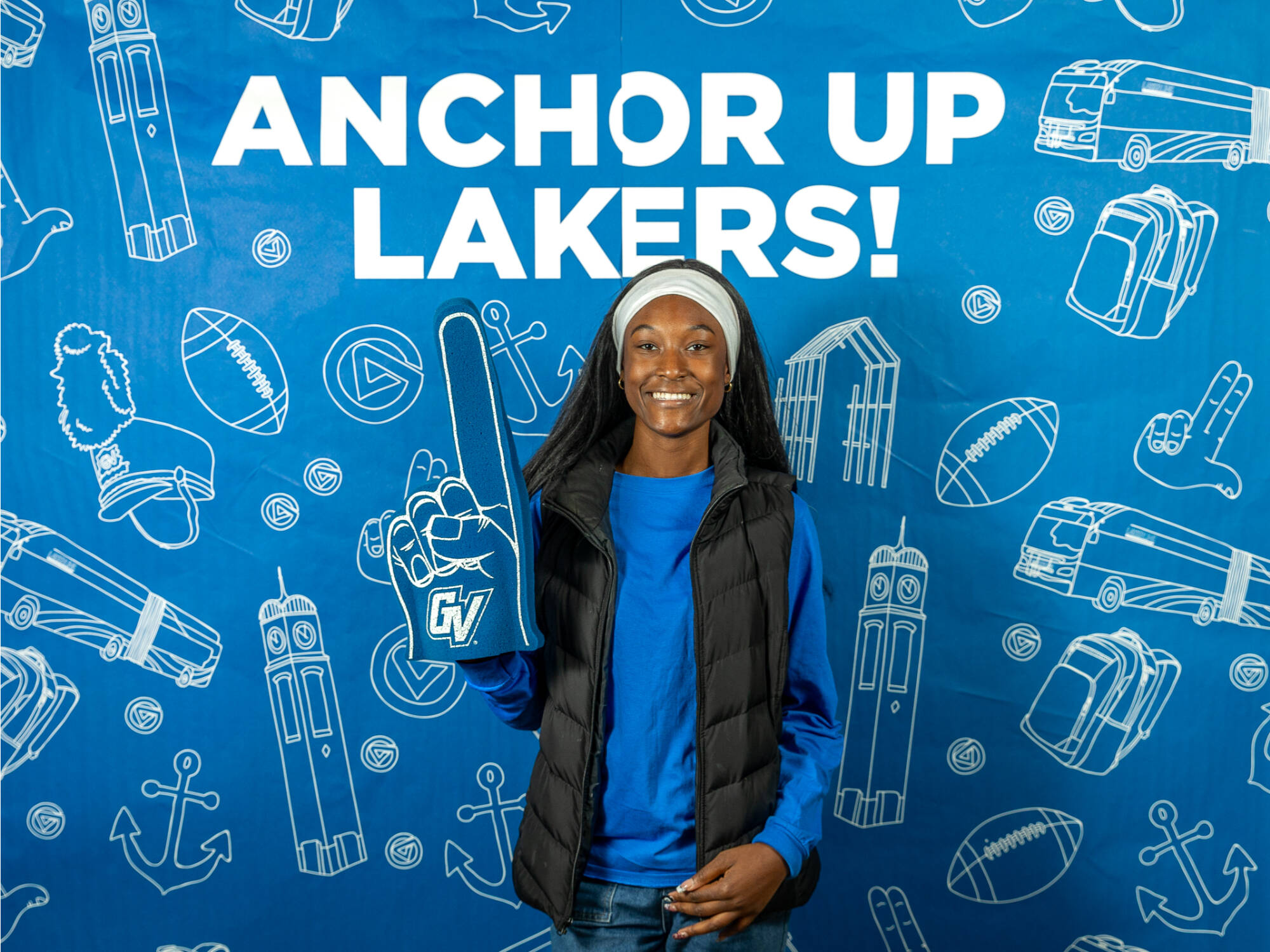 An individual holding up a GVSU foam finger wearing a black vest